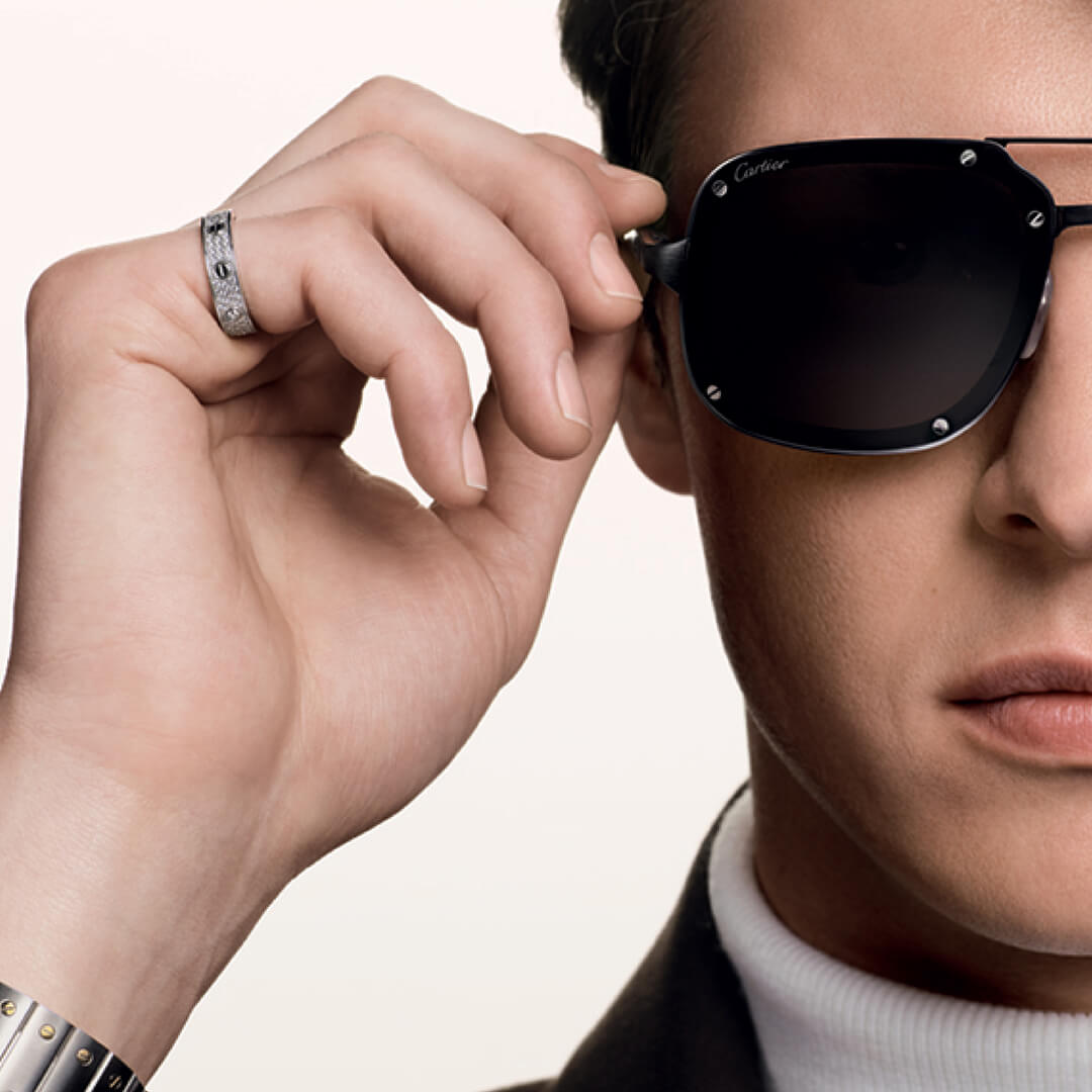 Person adjusting a pair of Cartier sunglasses with a neutral background